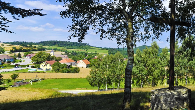 View of a rural community with church and houses, surrounded by fields and trees.