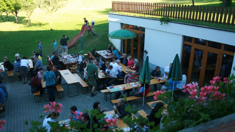 People sit at tables outside, surrounded by greenery and flowers.