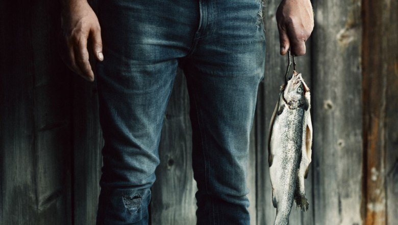 Person holding a trout in front of a wooden wall.