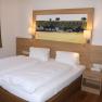 A guest room with a double bed, wooden paneling, bedside table and a picture of vineyards on the wall.