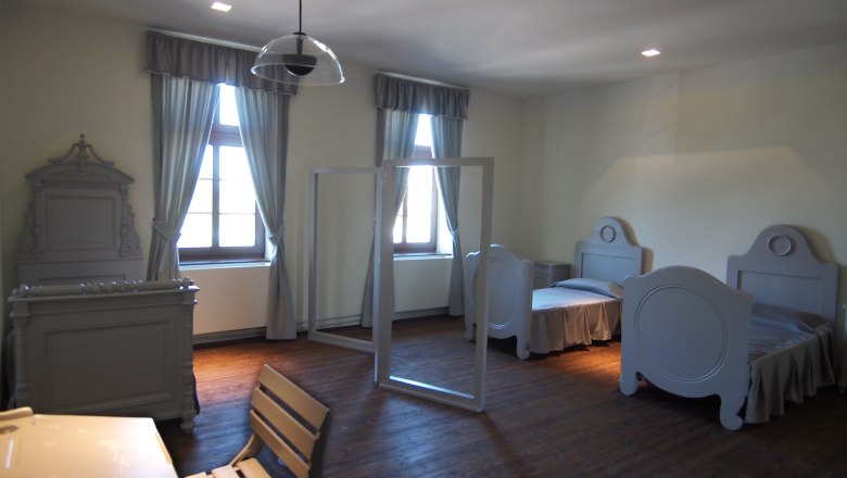 A simply furnished bedroom with two beds, a table and chairs, all in gray tones.