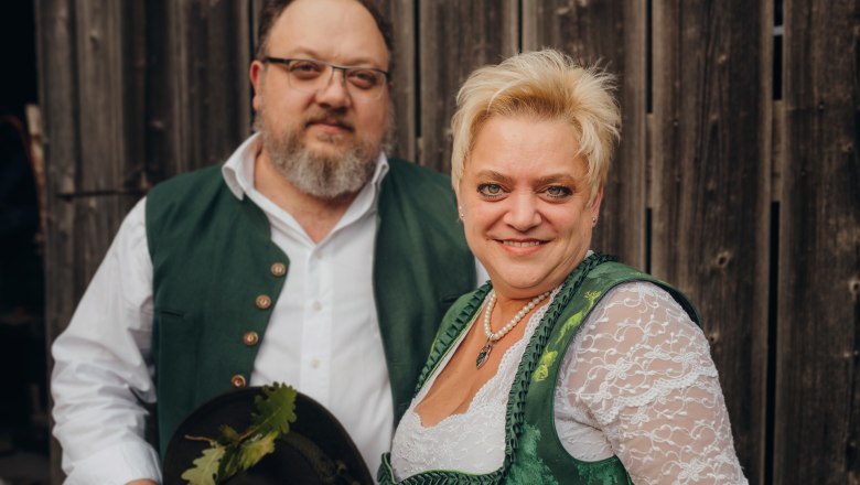 A man and a woman in traditional costume in front of a wooden wall.