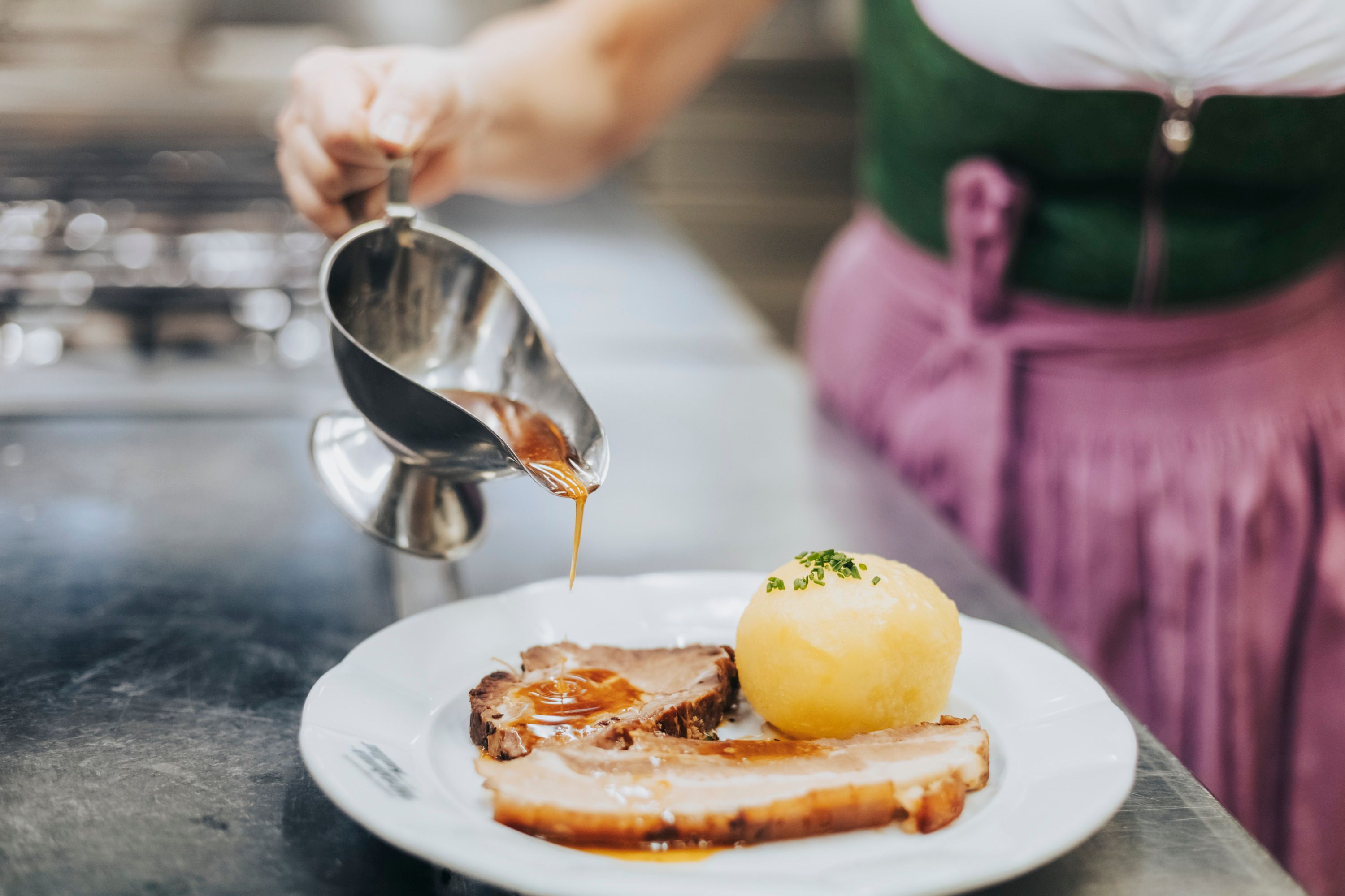 One person pours gravy over a plate of roast and dumplings.