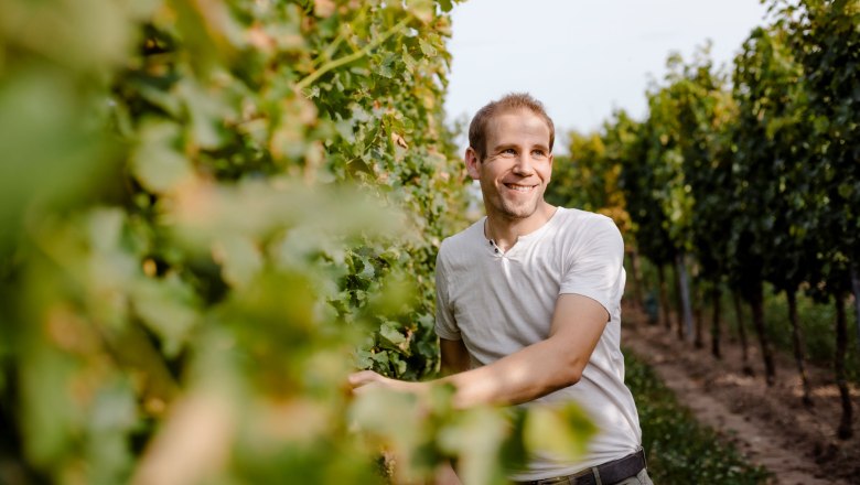 A man in a vineyard, smiling as he stands among the vines.