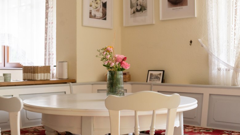 Dining area in a vacation home with round table, bouquet of flowers in a vase and decorative pictures on the wall.