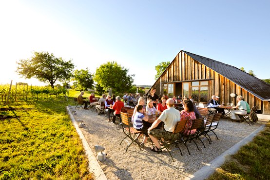 People sit at tables in front of a modern wooden building outside.