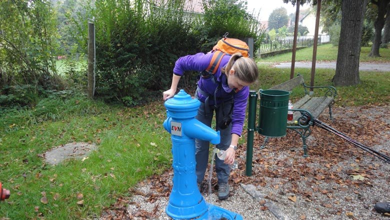 A person fills up a bottle at a blue drinking fountain outside.