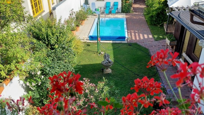 View of a garden with pool, surrounded by houses and red flowers in the foreground.