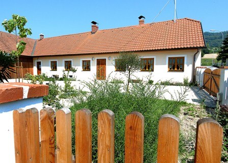 A white vacation home with a red tiled roof and wooden fence in the foreground.