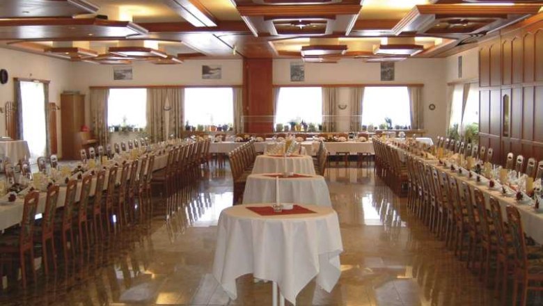 A large, elegantly decorated hall with long, laid tables and seating for over 200 people.