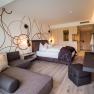 Modernly furnished hotel room with double bed, sofa and desk.