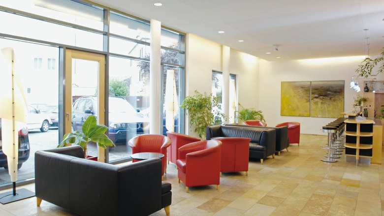 Bright hotel lobby with red and black armchairs, bar stools and large windows.