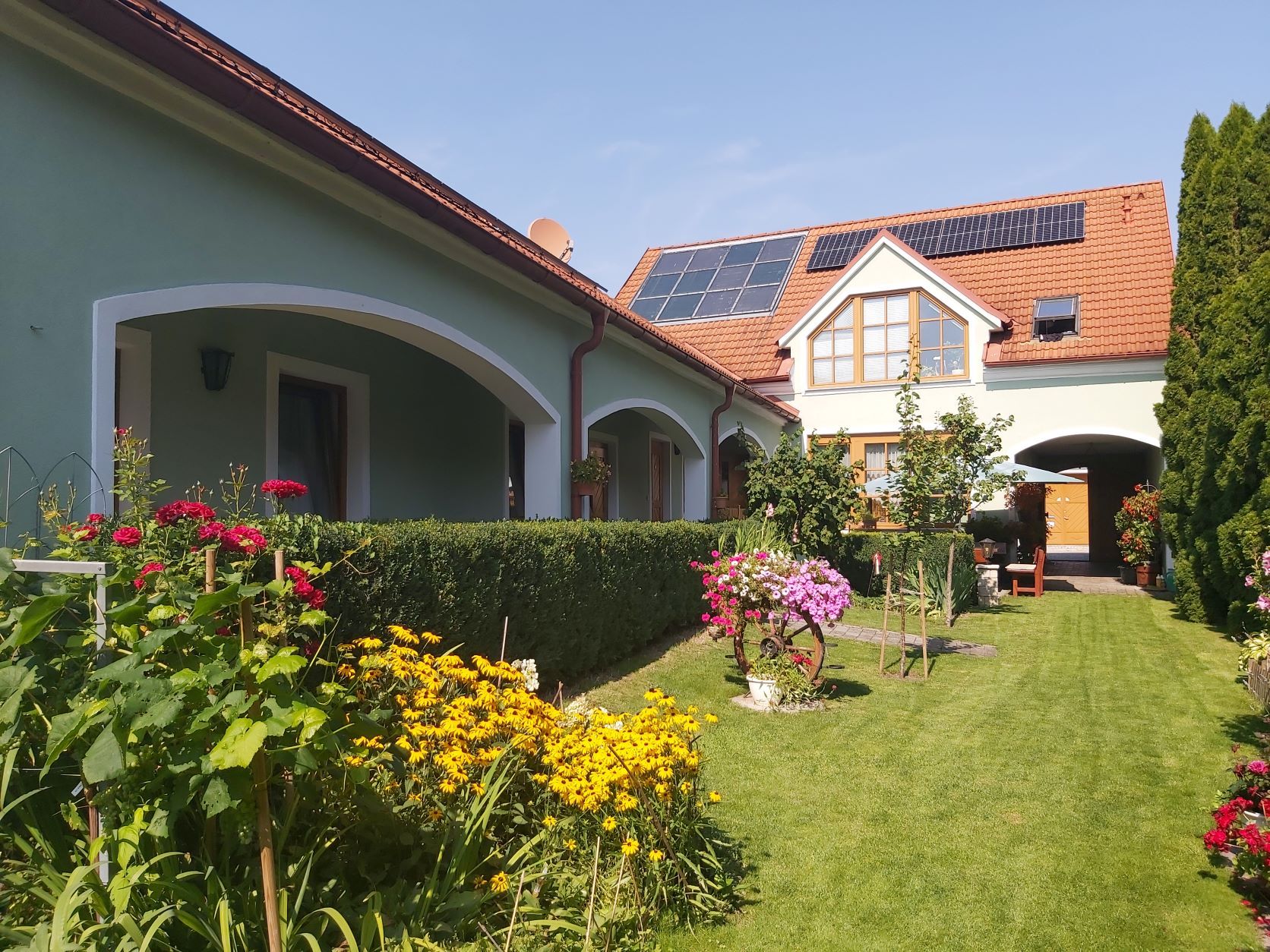 A well-tended garden with colorful flowers and a house with solar panels on the roof.