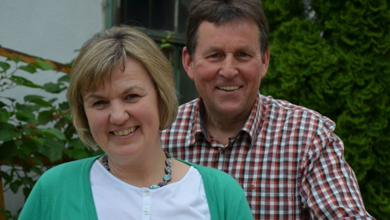 A smiling couple stands outside in front of a green hedge.