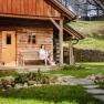 Woman in bathrobe sitting on a bench in front of a wooden hut in the countryside.