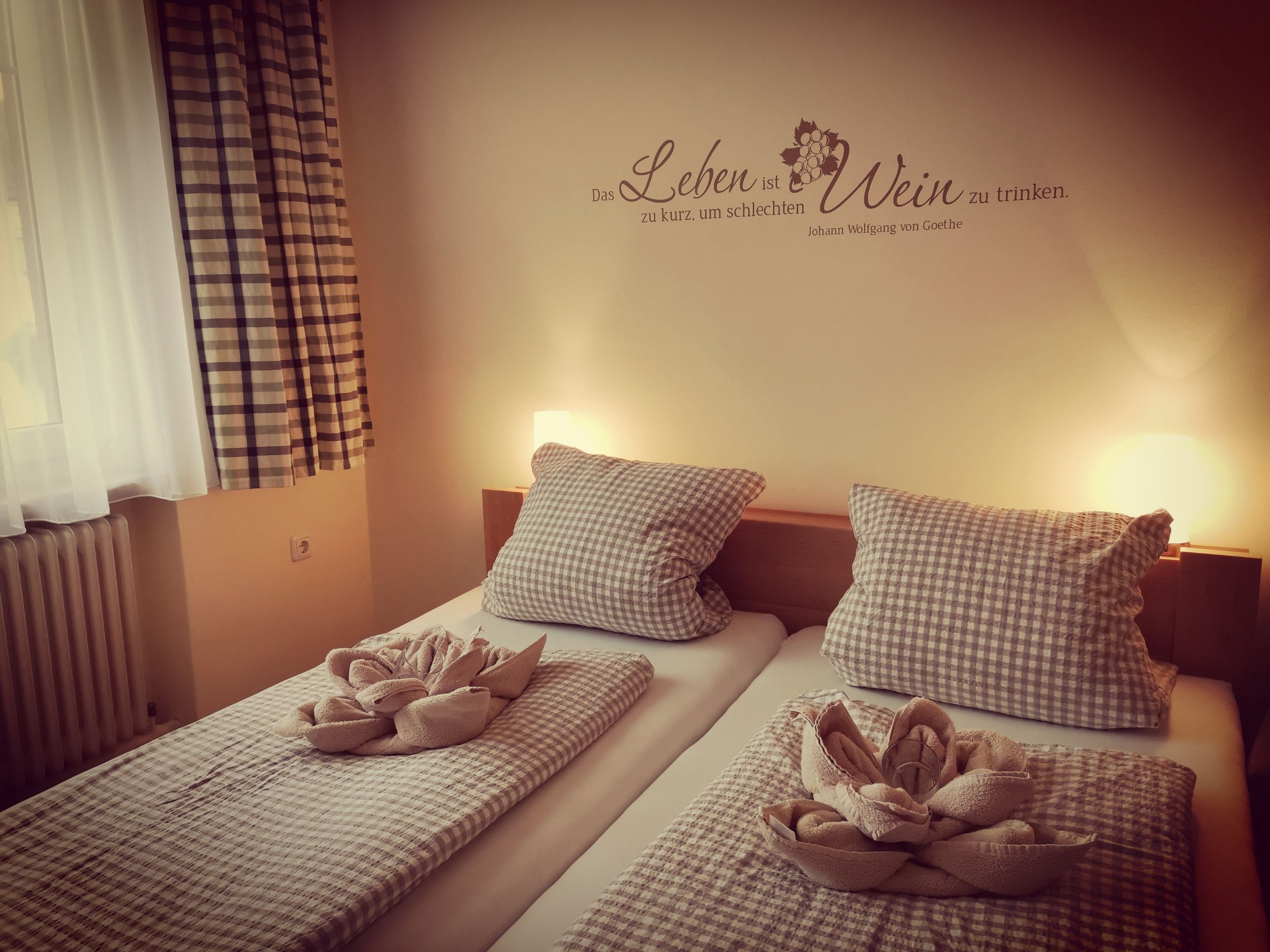 Cozy guest room with two beds, checkered comforters and pillows, decorative towels and a Goethe quote on the wall.