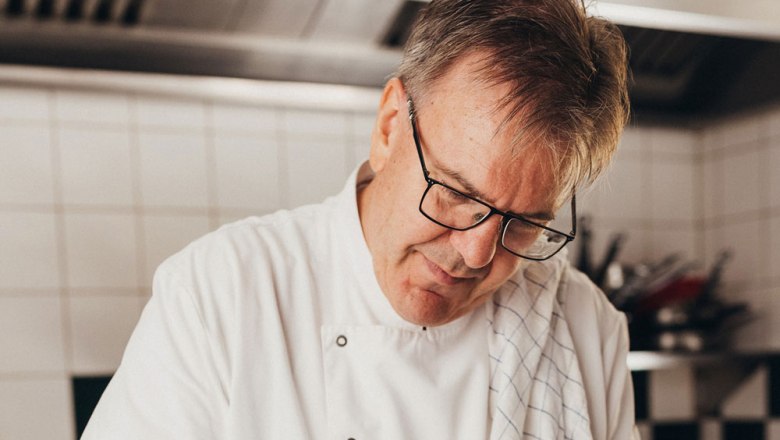 A chef in a white uniform works intently in a kitchen.