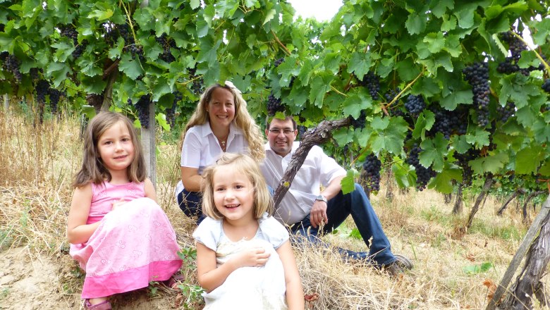 Family sits in a vineyard, surrounded by green leaves and grapes.