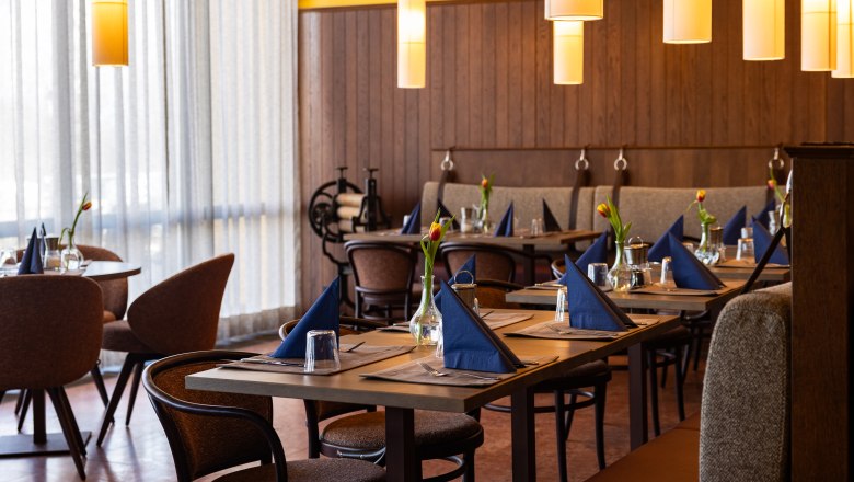 A stylishly furnished restaurant with laid tables, blue napkins and tulips in vases.