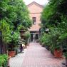 A paved courtyard with plants in pots and a brick building in the background.