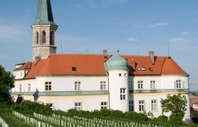 Gumpoldskirchen Castle with its red roof and tower, surrounded by vineyards under a blue sky.
