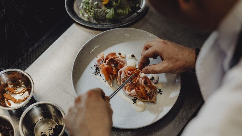 Chef decorates a dish with salmon and vegetables on a plate.