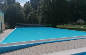 An empty outdoor swimming pool surrounded by trees and a building.