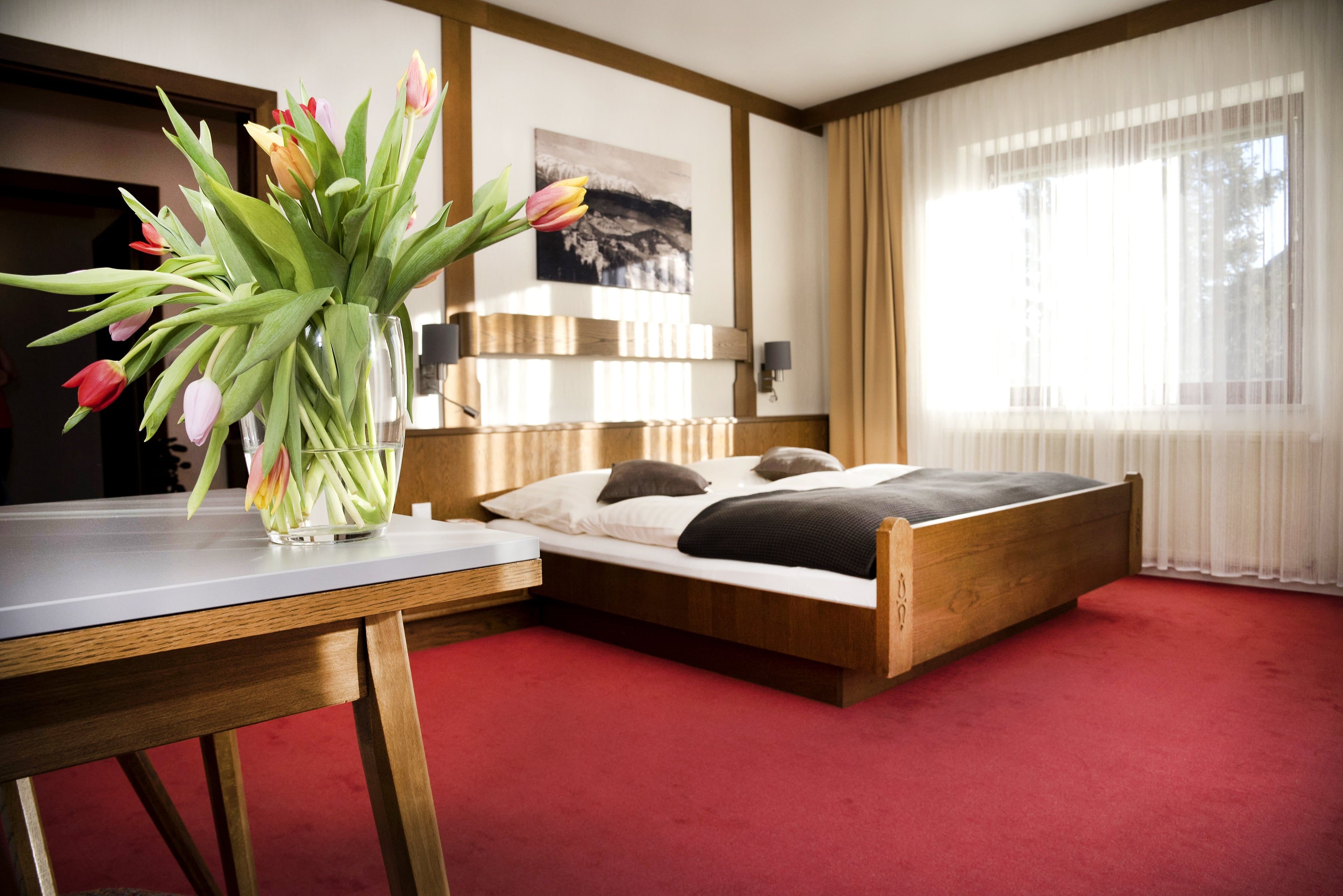 A cozy double room with a wooden bed, red carpet and a table with a bouquet of tulips.