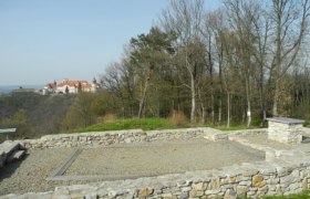 Ruins of an old stone wall with a castle in the background on a hill.