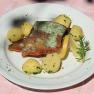 A plate of fried trout fillet, potatoes, lemon slices and herbs on a pink tablecloth.
