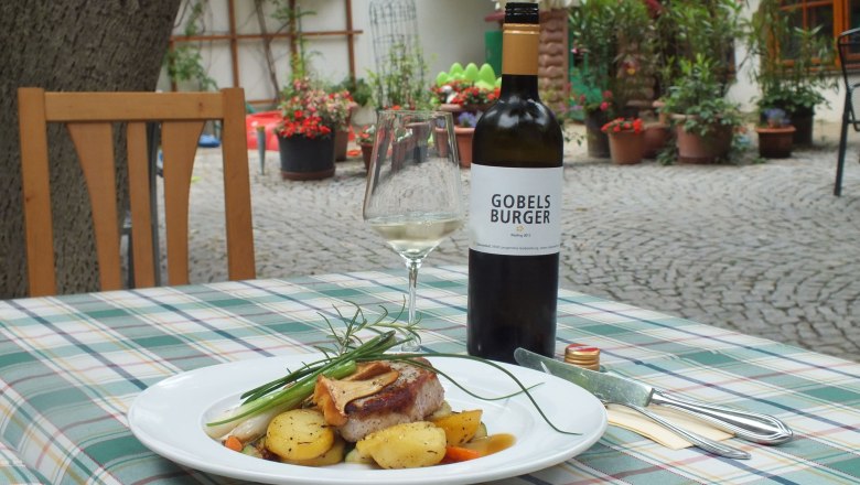 A plate of meat and potatoes on an outdoor table, with a bottle of wine and a glass next to it.