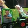Three children playing in the garden with a toy tractor and trailer.