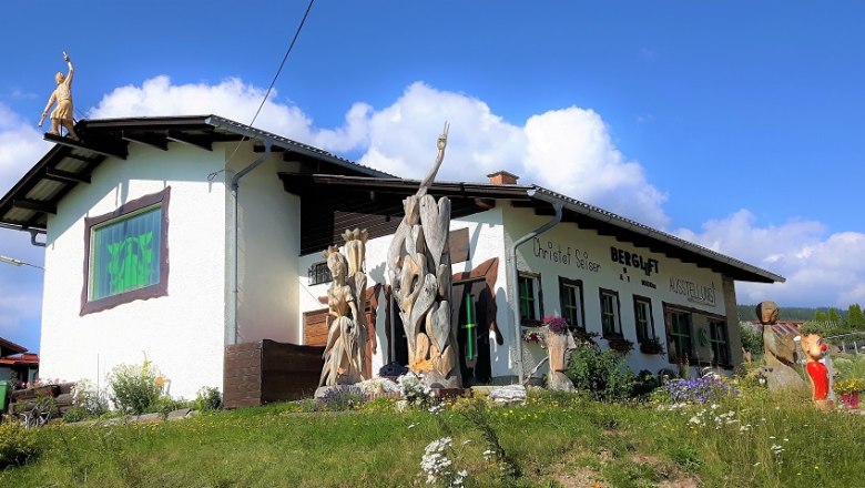 A building with the inscription 'Bergluft' and wooden sculptures in the foreground.