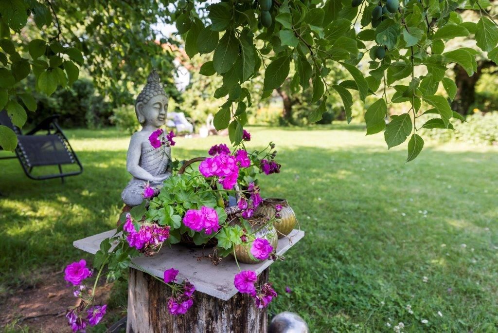 Garden with Buddha statue and pink flowers on a wooden stump.