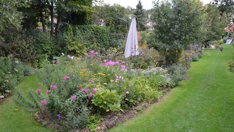 A cottage garden with colorful flowers, a closed sunshade and a well-tended lawn.