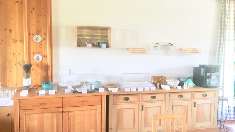 Breakfast buffet on a wooden buffet with dishes, glasses and a coffee machine.