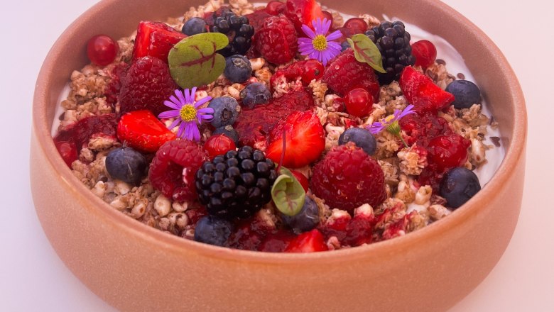 Bowl with yogurt, muesli, berries and edible flowers.