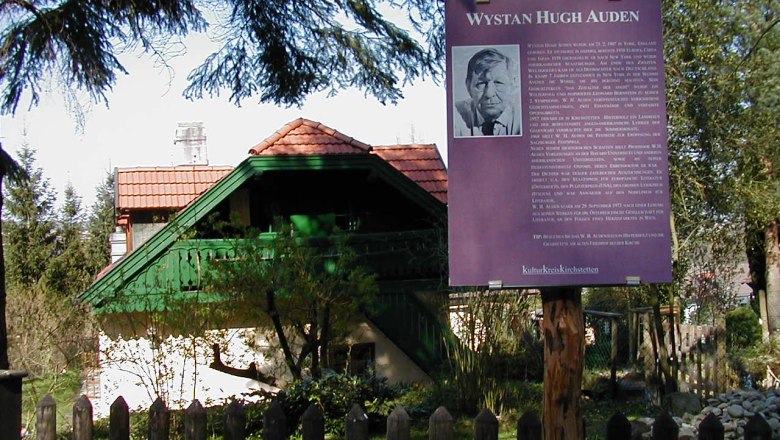 W.H. Auden memorial with information board and house in the background.
