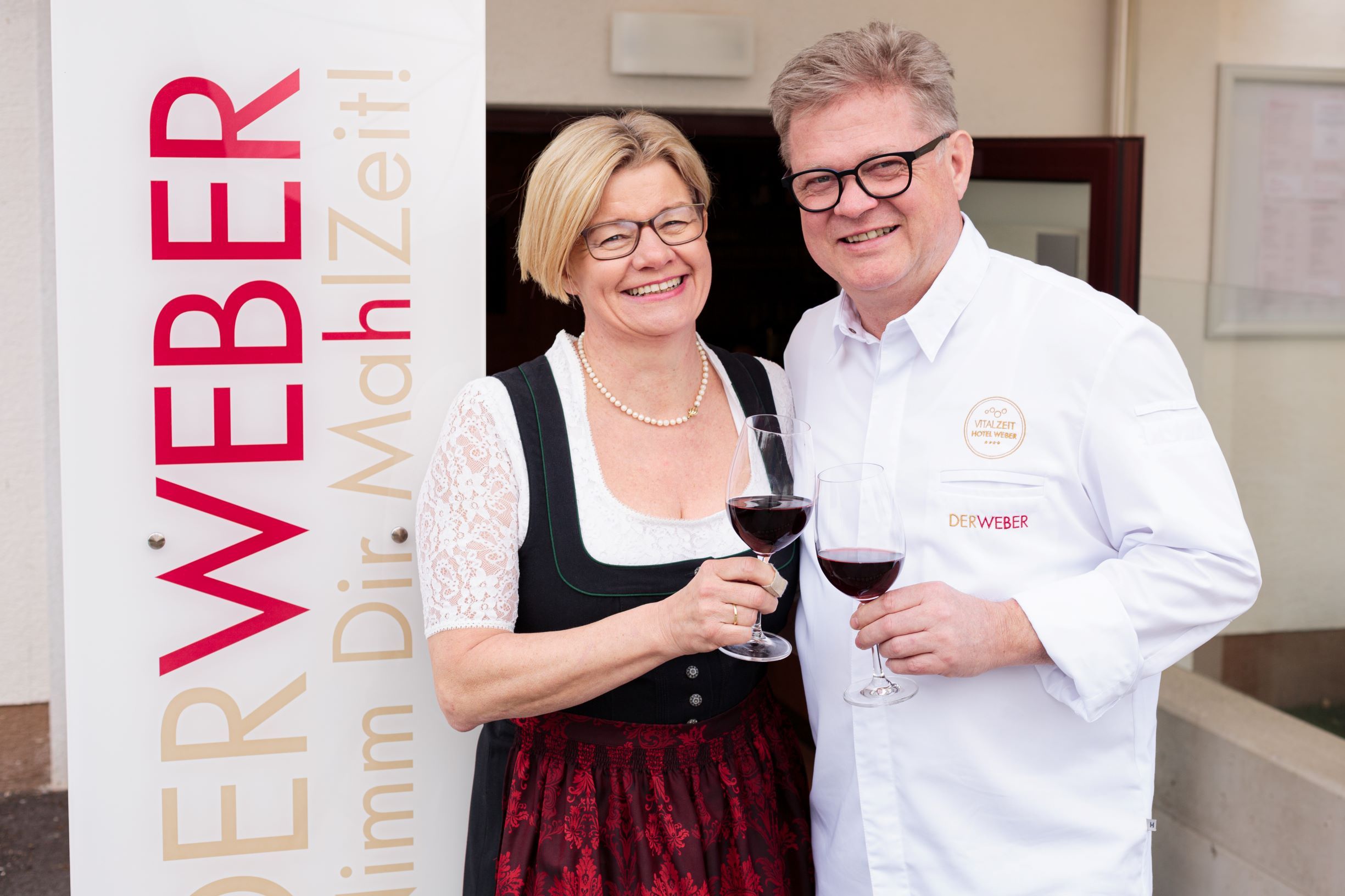A man and a woman clink glasses of wine next to a sign that reads 'The Weaver'.