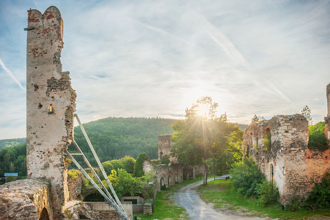 Ruins of Gars Castle at sunset with wooded hills in the background.