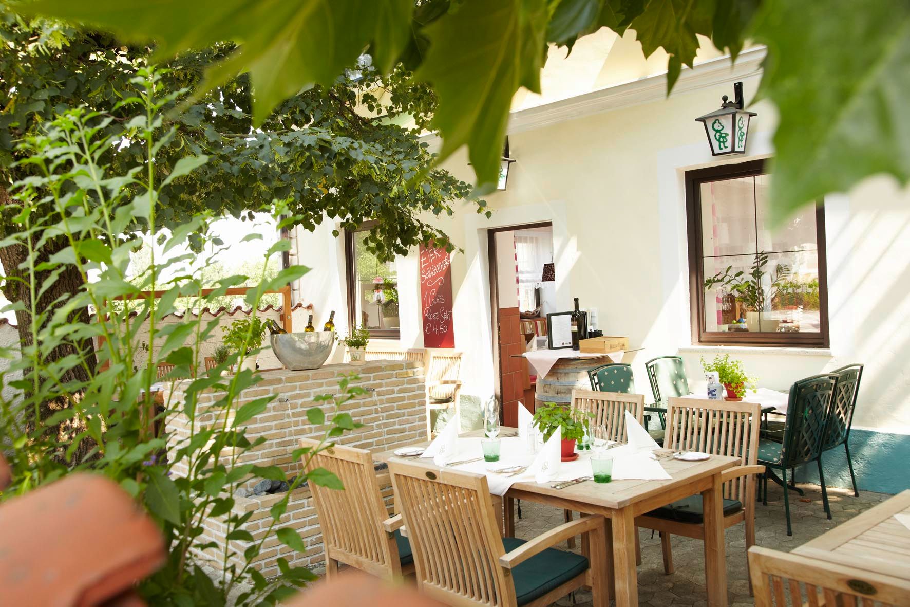 A cozy guest garden with wooden tables and chairs, surrounded by plants and trees.