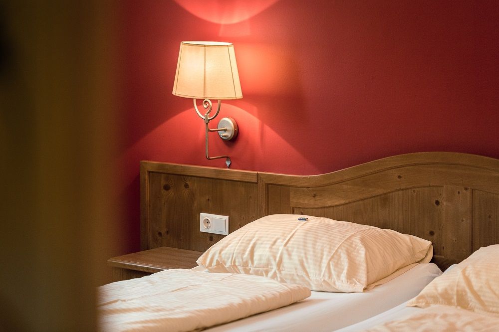 A cozy double room with wooden headboard, red wall and wall lamp.