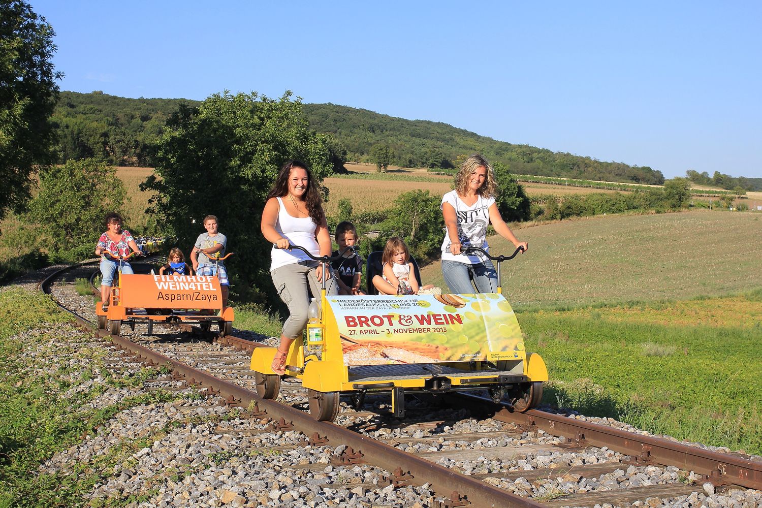 People ride on a trolley through a rural landscape.