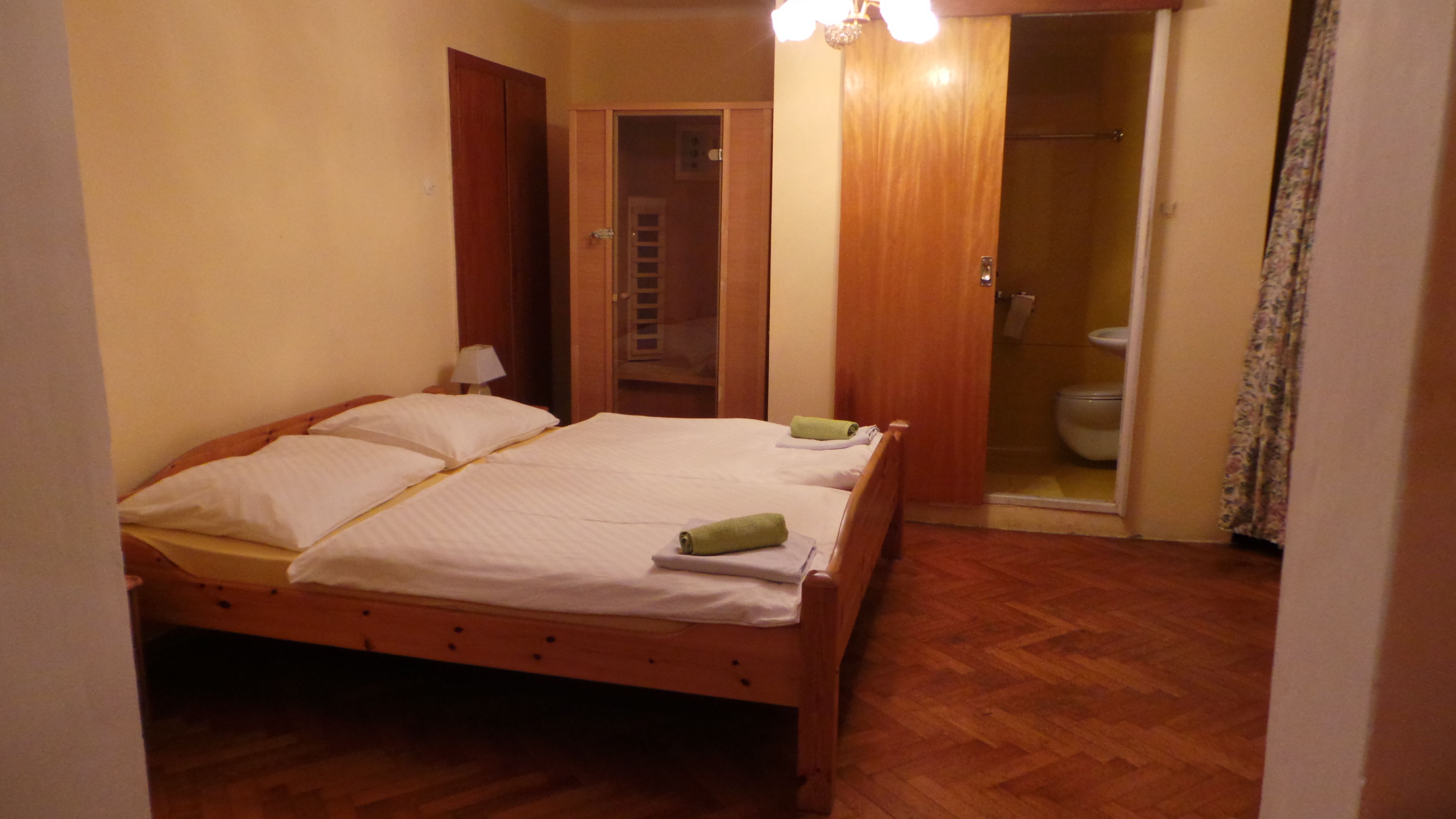 A simply furnished hotel room with a double bed, wooden floor and small bathroom.