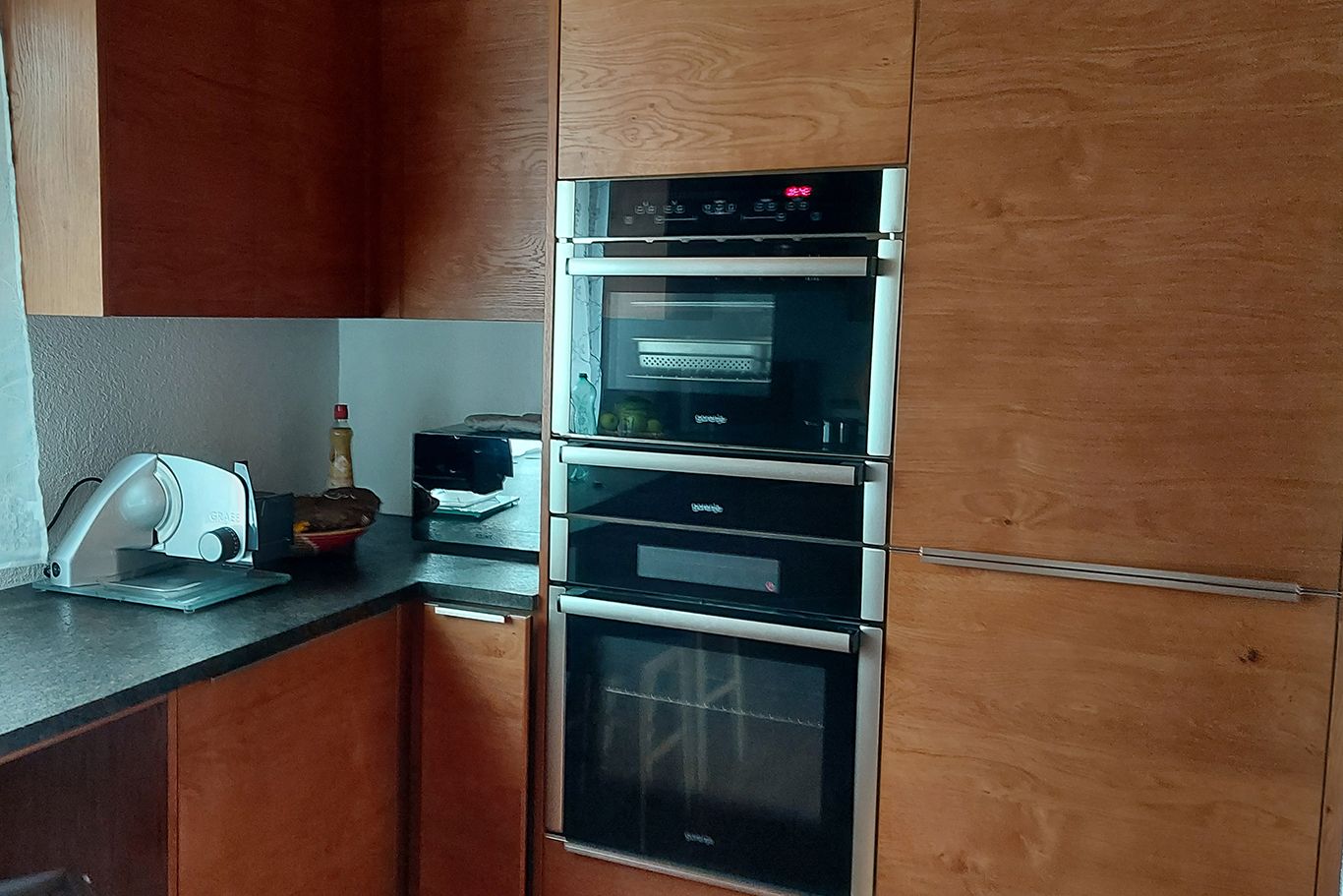 Modern kitchen with wooden cupboards, built-in oven and worktop with kitchen appliances.
