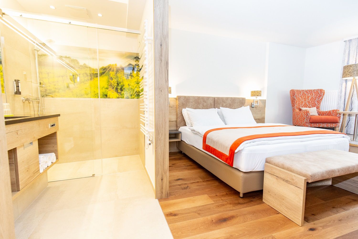 Modern hotel room with double bed, orange armchair and open shower.
