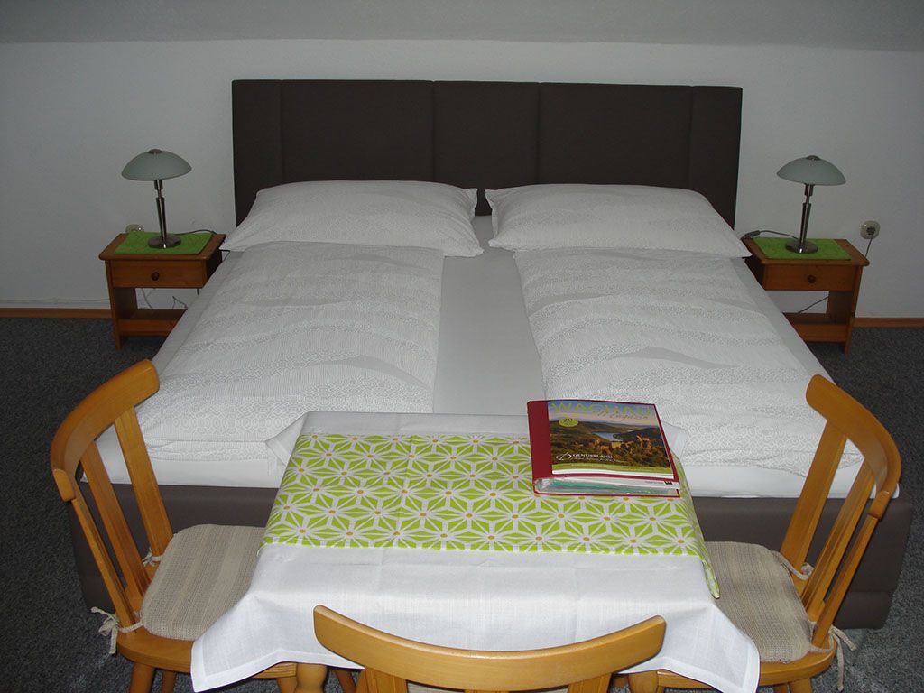 A double bed with white comforters, two bedside tables with lamps and a small table with two chairs in the foreground.