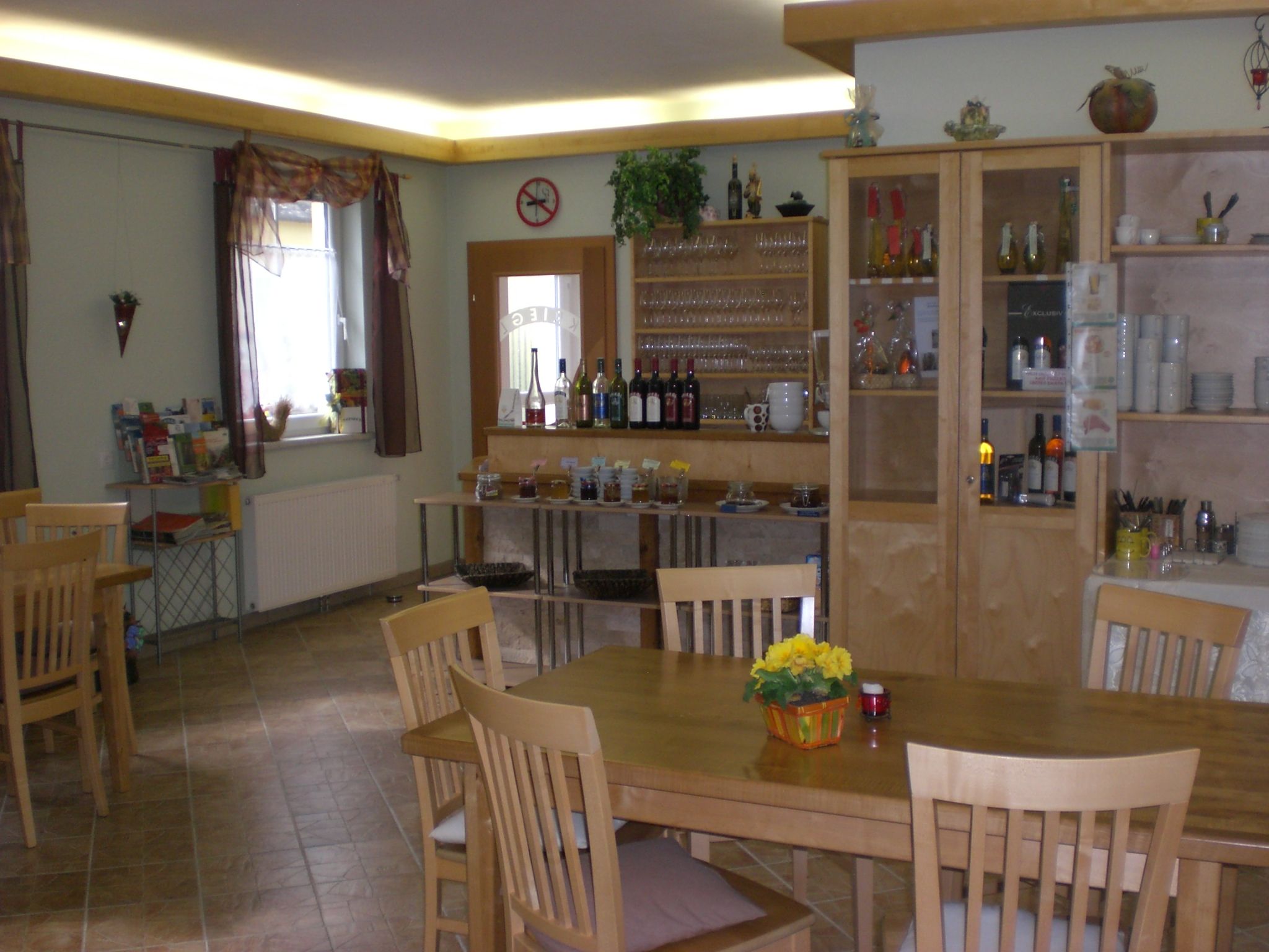 A cozy tasting and breakfast room with wooden furniture, shelves with glasses and bottles, and a table with flowers.