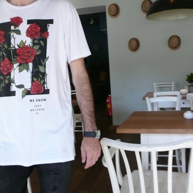 Person in a white T-shirt with a rose motif in a café.