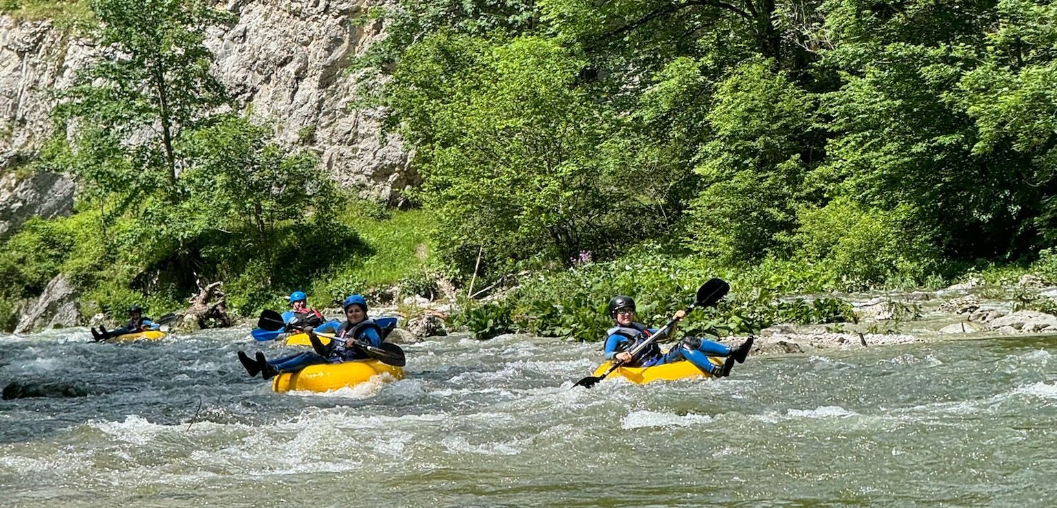 People tubing on a river in a green, wooded setting.